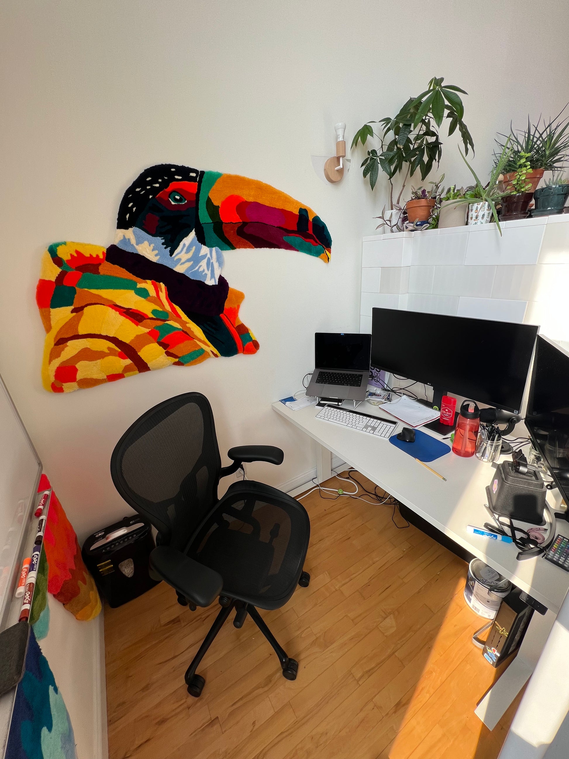 Home office with colorful toucan hanging rug, office chair, and desk setup.