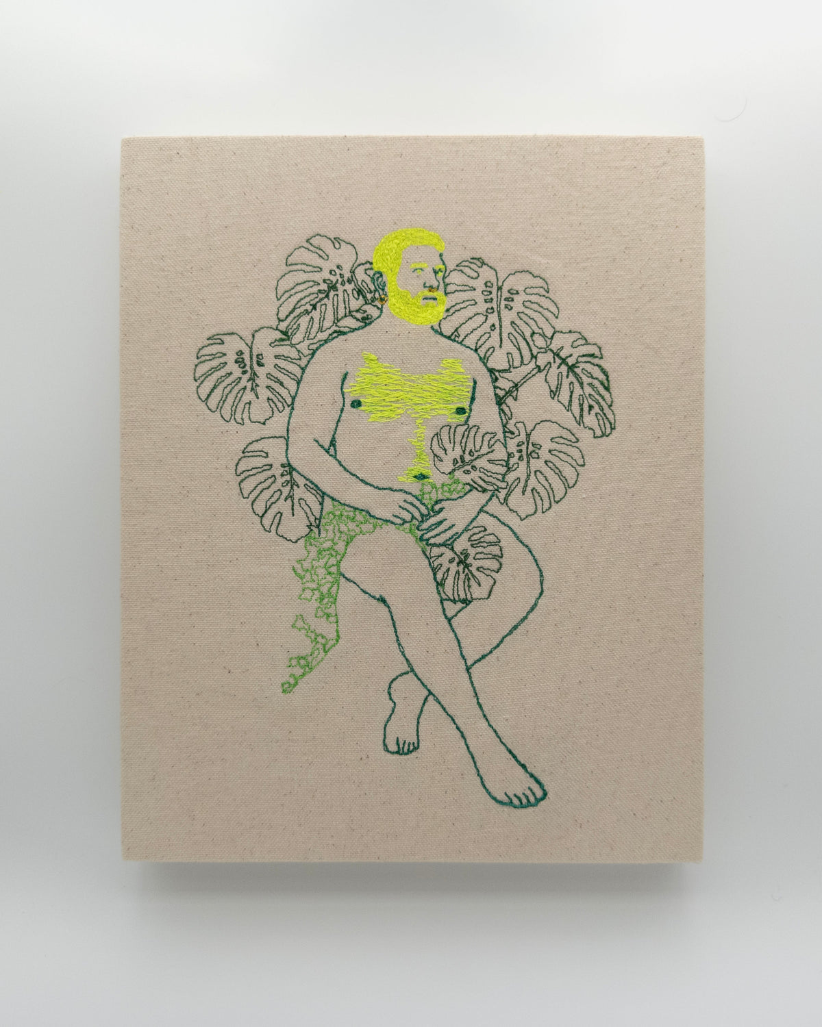 Amarelo: embroidered figure with a neon yellow beard, legs crossed, framed by monstera leaves, on natural canvas