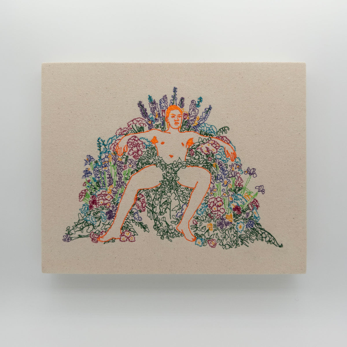 Ari: embroidered figure outlined in orange, arms spread across an arch of flowers, on natural canvas