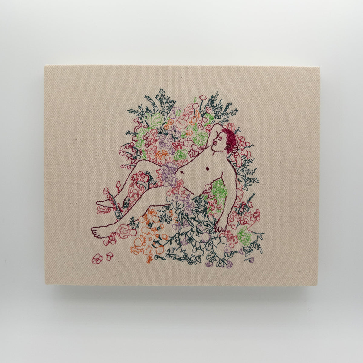 Rosso: embroidered figure with crimson hair reclining in a bed of flowers, on natural canvas