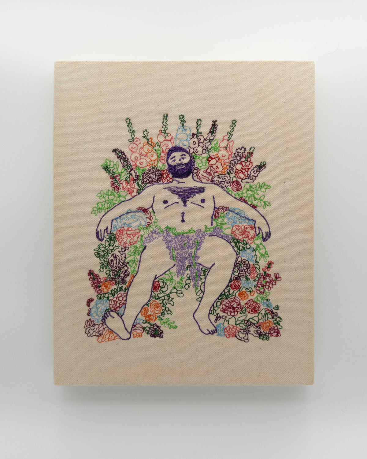 Ube: embroidered figure with a deep purple beard, arms spread wide over a field of flowers, on natural canvas